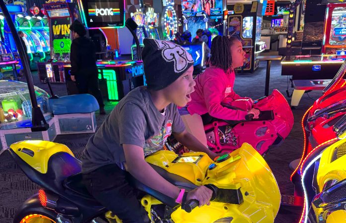  Two students playing a racing game at Dave and Busters